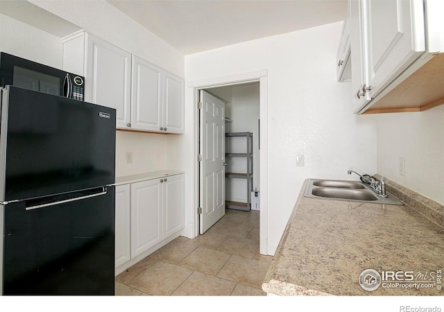 kitchen featuring light tile patterned floors, white cabinetry, black fridge, and sink