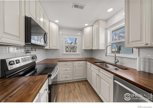 kitchen featuring appliances with stainless steel finishes, white cabinetry, sink, and butcher block counters