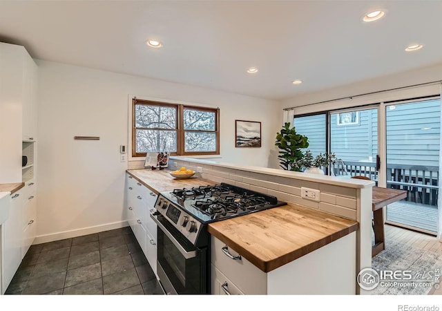 kitchen featuring white cabinetry, wood counters, stainless steel gas range, kitchen peninsula, and decorative backsplash