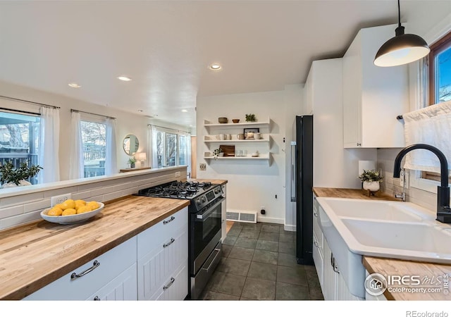 kitchen with decorative light fixtures, white cabinetry, stainless steel range with gas cooktop, and wooden counters