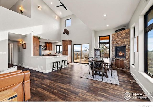 dining area with dark wood-style floors, a stone fireplace, recessed lighting, and baseboards