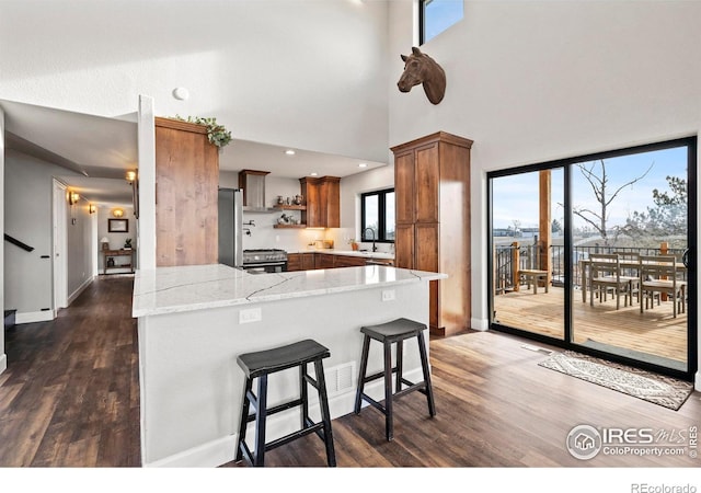 kitchen featuring dark wood finished floors, open shelves, stainless steel appliances, brown cabinetry, and a peninsula