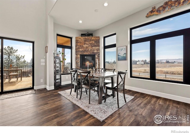 dining room with dark wood-style floors, baseboards, a stone fireplace, and recessed lighting