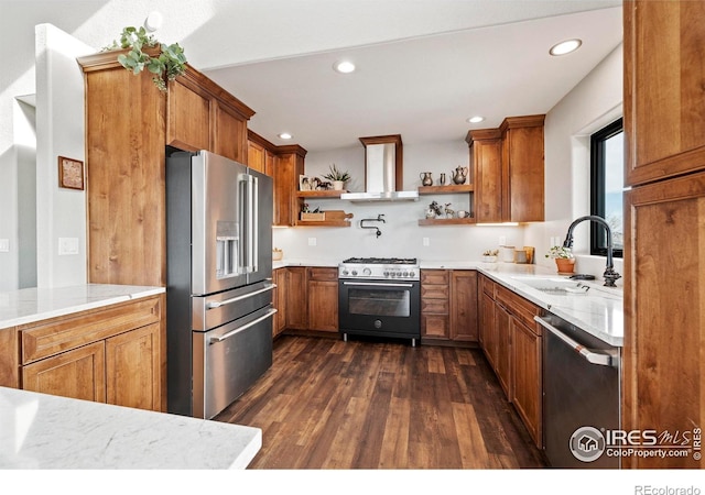 kitchen with premium appliances, open shelves, brown cabinetry, a sink, and wall chimney range hood