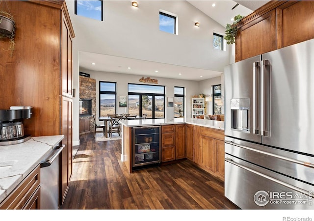 kitchen with dark wood-style floors, appliances with stainless steel finishes, brown cabinetry, beverage cooler, and a peninsula