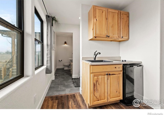 kitchen with baseboards, wine cooler, dark wood-type flooring, light brown cabinets, and a sink