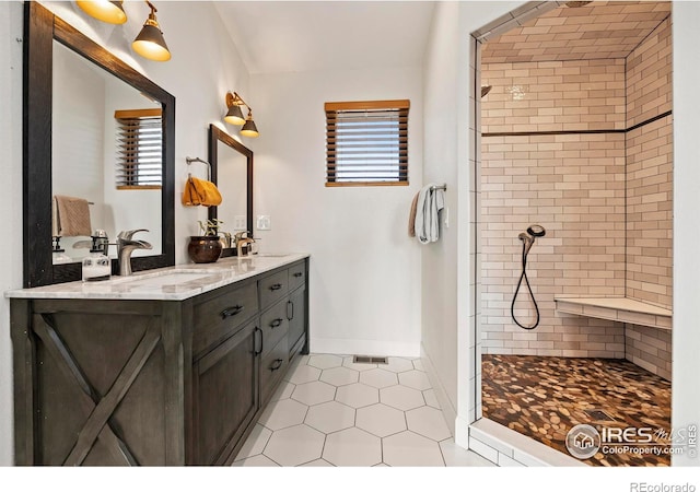 full bath featuring tile patterned flooring, tiled shower, a sink, and double vanity