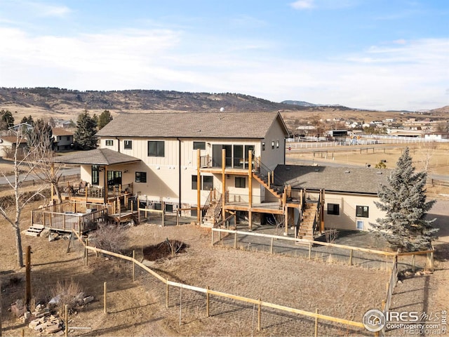 rear view of property featuring a shingled roof, fence, a deck with mountain view, and stairs