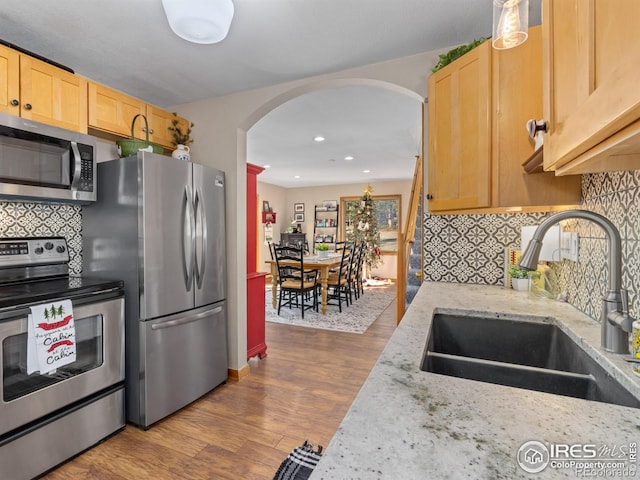 kitchen featuring sink, tasteful backsplash, light stone counters, wood-type flooring, and stainless steel appliances