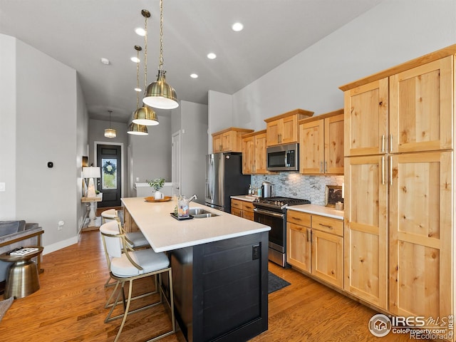 kitchen with pendant lighting, light brown cabinets, backsplash, a center island with sink, and stainless steel appliances