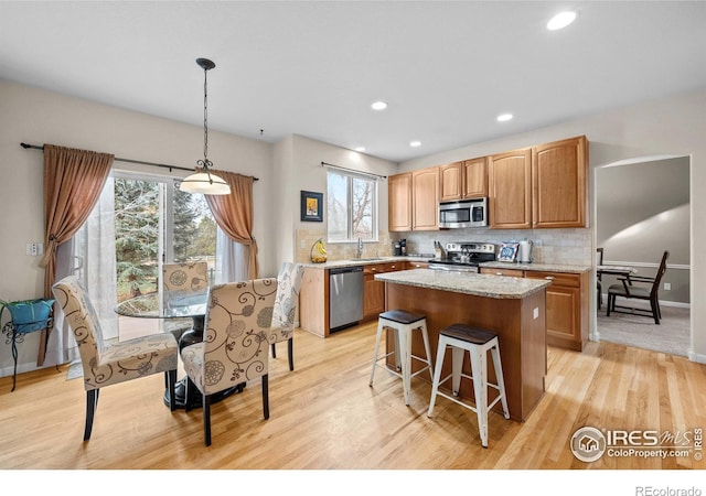 kitchen with a center island, hanging light fixtures, stainless steel appliances, decorative backsplash, and light wood-type flooring