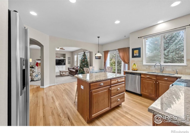 kitchen with a center island, sink, hanging light fixtures, stainless steel appliances, and tasteful backsplash