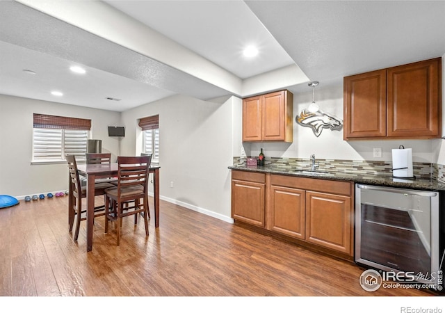 kitchen featuring sink, hanging light fixtures, dark wood-type flooring, beverage cooler, and dark stone counters