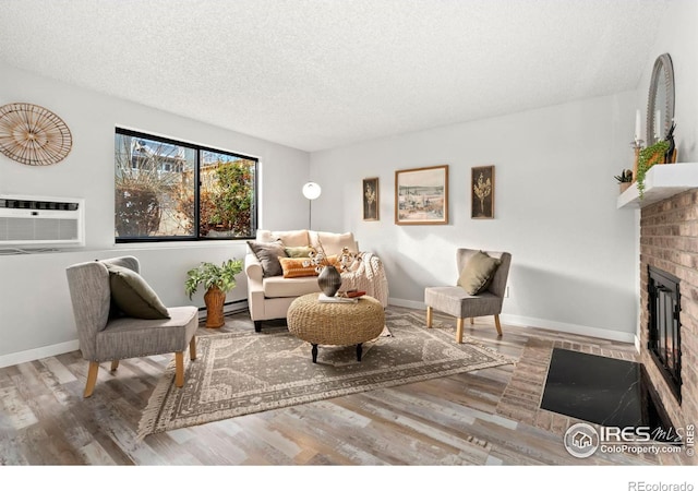 living room with a baseboard heating unit, a brick fireplace, hardwood / wood-style flooring, a textured ceiling, and a wall mounted AC