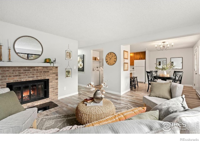 living room with washer and clothes dryer, light hardwood / wood-style floors, a textured ceiling, and a brick fireplace