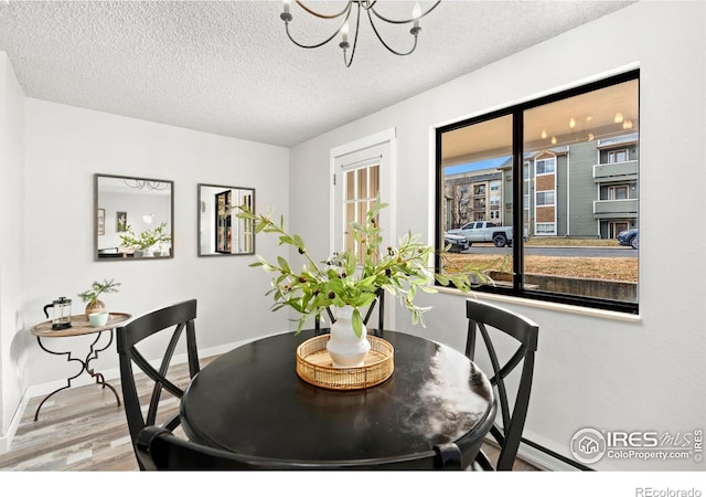 dining area with hardwood / wood-style floors, a textured ceiling, and an inviting chandelier