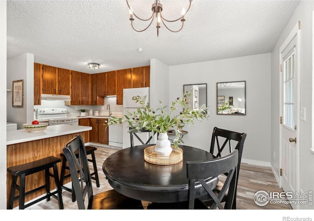 dining room with light hardwood / wood-style flooring, sink, a textured ceiling, and an inviting chandelier