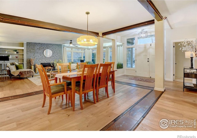 dining space with beam ceiling, ceiling fan, built in features, a fireplace, and light wood-type flooring