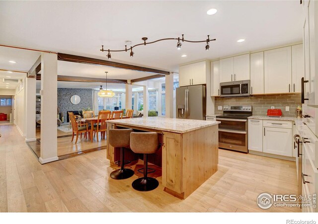 kitchen featuring white cabinets, light stone countertops, decorative light fixtures, a kitchen island, and stainless steel appliances