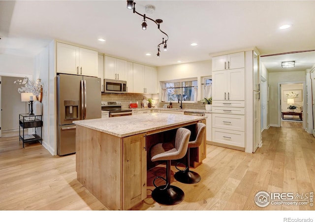 kitchen with white cabinets, a kitchen island, stainless steel appliances, and light hardwood / wood-style flooring