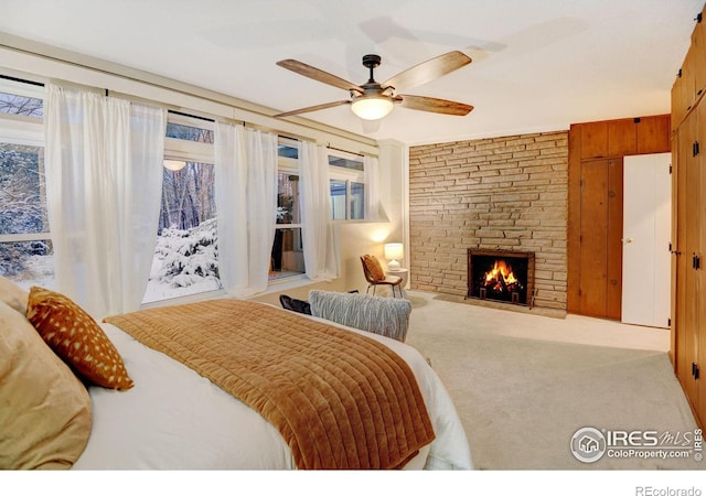 carpeted bedroom with a fireplace, multiple windows, ceiling fan, and wood walls