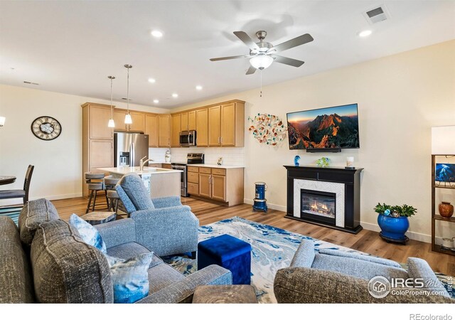 living room with ceiling fan, light hardwood / wood-style flooring, and sink