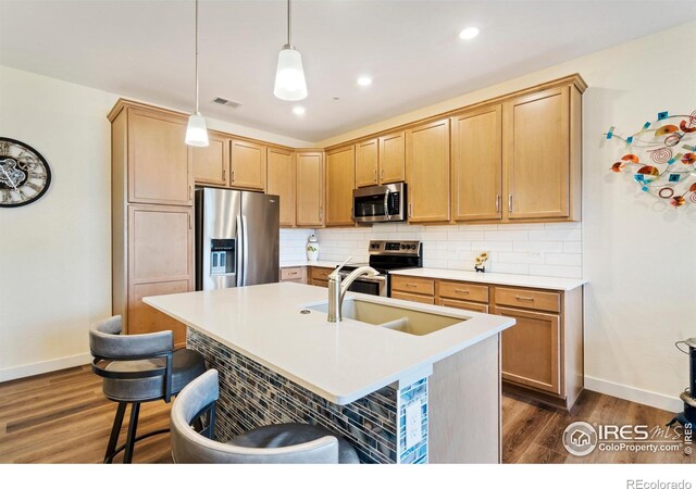 kitchen with a kitchen island with sink, hanging light fixtures, sink, appliances with stainless steel finishes, and dark hardwood / wood-style flooring