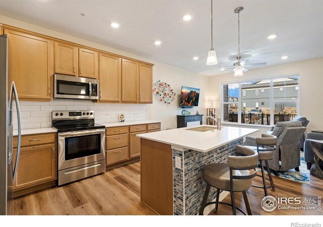 kitchen with pendant lighting, a kitchen island with sink, ceiling fan, light wood-type flooring, and stainless steel appliances