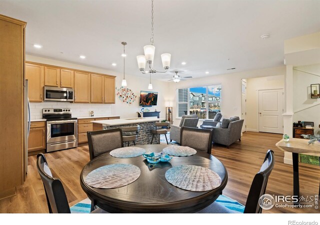 dining area with light hardwood / wood-style flooring, ceiling fan with notable chandelier, and sink