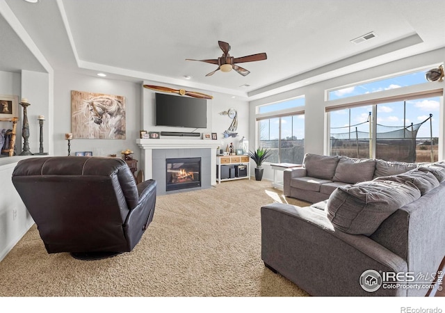 carpeted living room with ceiling fan, a fireplace, and a tray ceiling