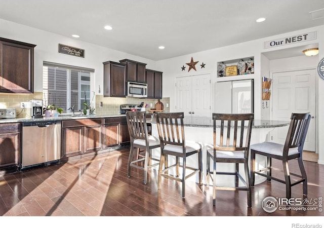 kitchen featuring light stone counters, stainless steel appliances, decorative backsplash, a kitchen island, and a breakfast bar area