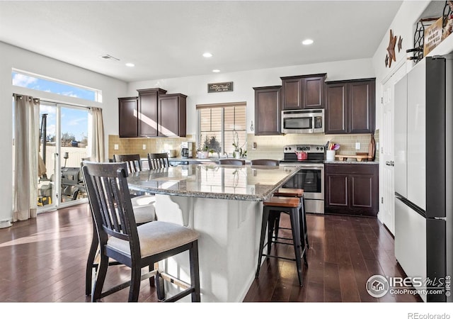 kitchen featuring appliances with stainless steel finishes, a center island, light stone countertops, a breakfast bar, and dark hardwood / wood-style floors