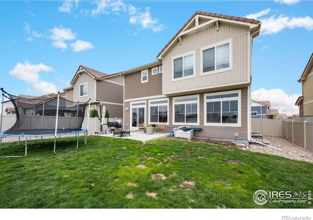 back of property with a lawn, a patio area, and a trampoline