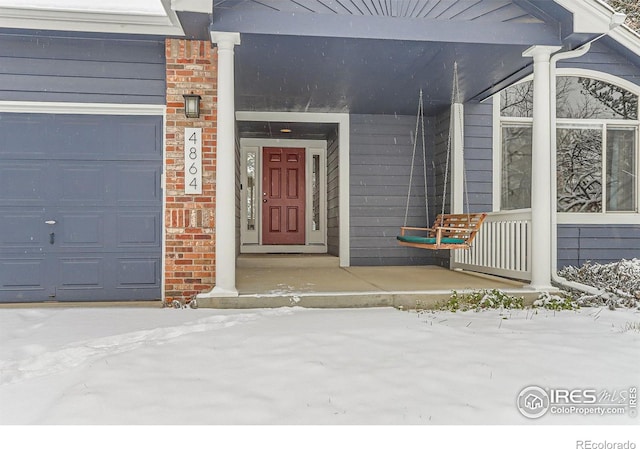 snow covered property entrance featuring a porch and a garage