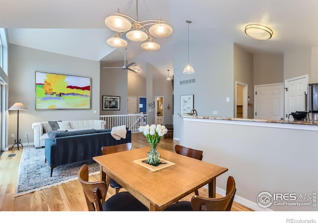 dining room with ceiling fan with notable chandelier, light hardwood / wood-style floors, and high vaulted ceiling