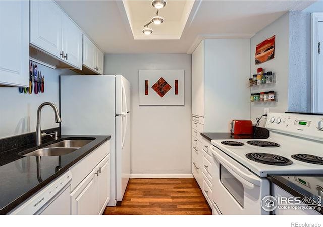 kitchen with white appliances, a tray ceiling, dark wood-type flooring, sink, and white cabinets