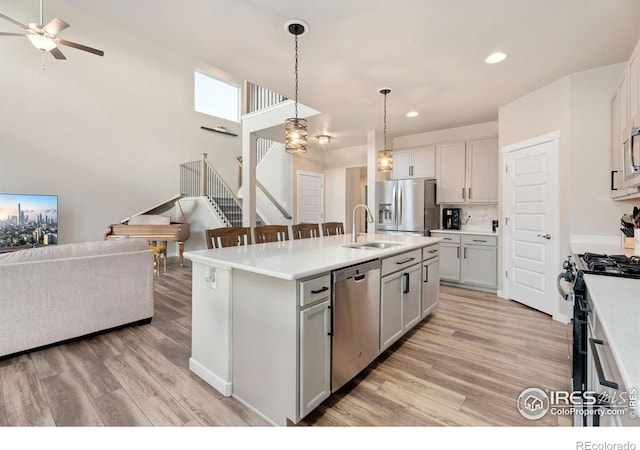 kitchen with sink, hanging light fixtures, light hardwood / wood-style flooring, appliances with stainless steel finishes, and a kitchen island with sink