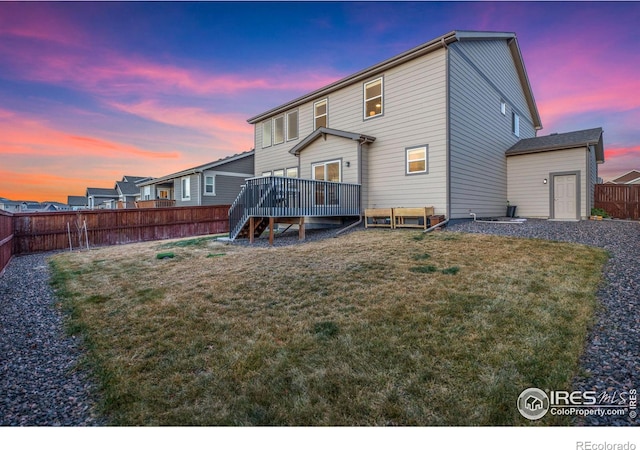 back house at dusk featuring a wooden deck and a yard