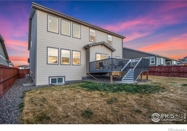 back house at dusk with a yard and a deck