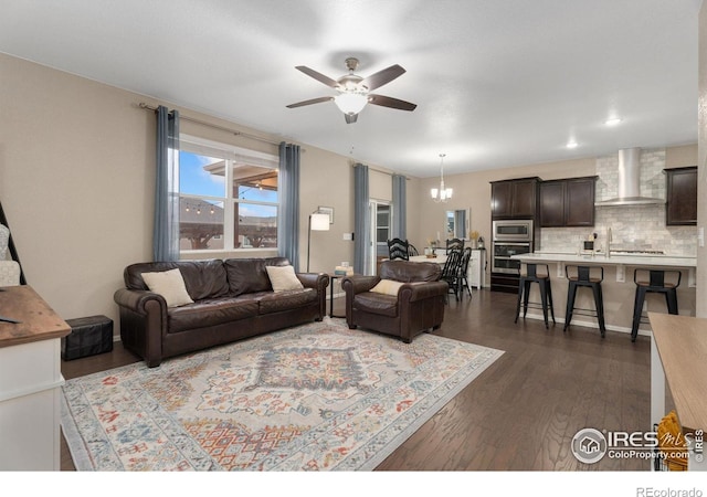 living room featuring ceiling fan with notable chandelier, sink, and dark wood-type flooring