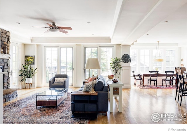 living room featuring a stone fireplace, crown molding, hardwood / wood-style flooring, ceiling fan, and a tray ceiling