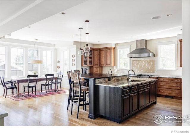 kitchen with decorative light fixtures, tasteful backsplash, wall chimney exhaust hood, and sink