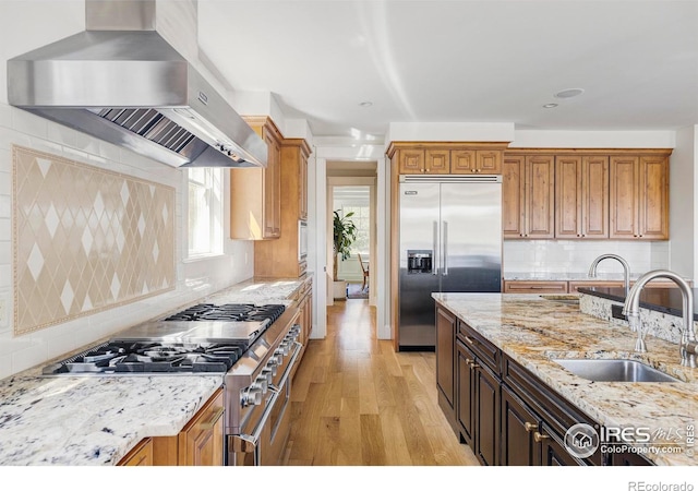 kitchen featuring wall chimney range hood, sink, light stone countertops, tasteful backsplash, and premium appliances