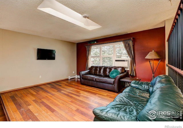 living room with a skylight, a textured ceiling, baseboard heating, cooling unit, and light hardwood / wood-style flooring