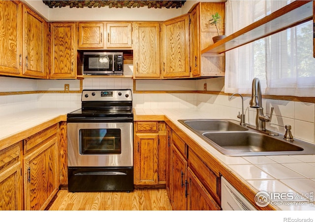 kitchen featuring appliances with stainless steel finishes, backsplash, sink, light hardwood / wood-style flooring, and tile counters