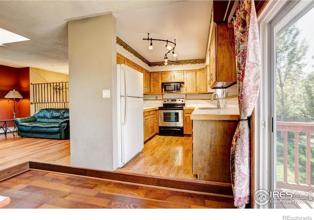 kitchen with sink, a textured ceiling, appliances with stainless steel finishes, light hardwood / wood-style floors, and kitchen peninsula