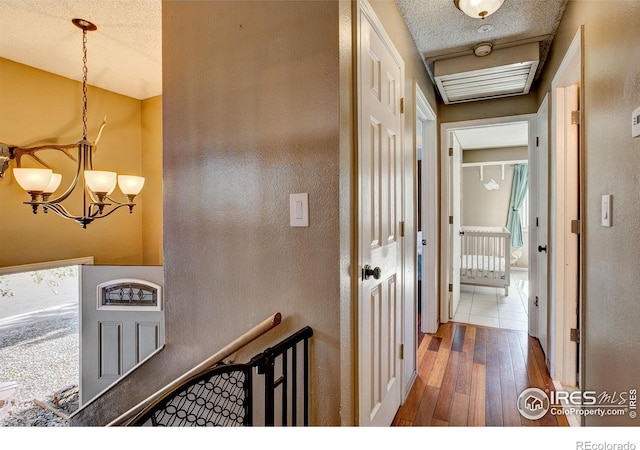 corridor with hardwood / wood-style flooring, a textured ceiling, and a chandelier