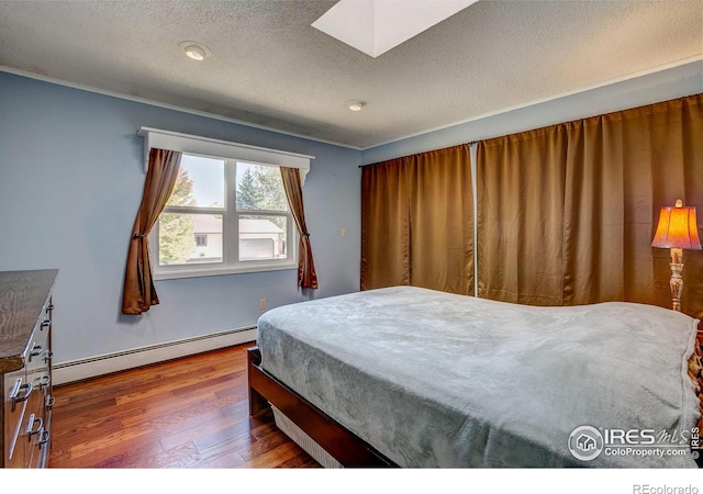 bedroom with hardwood / wood-style floors, a skylight, a textured ceiling, and a baseboard radiator