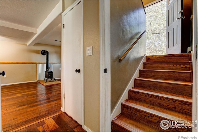 staircase with hardwood / wood-style flooring, beam ceiling, and a wood stove