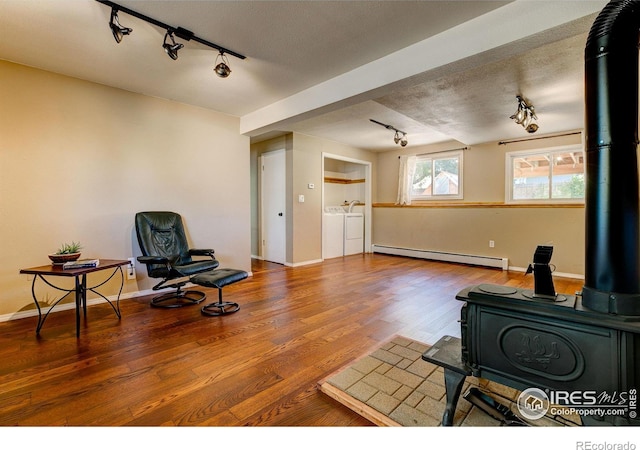 sitting room featuring a textured ceiling, baseboard heating, wood-type flooring, washing machine and dryer, and a wood stove